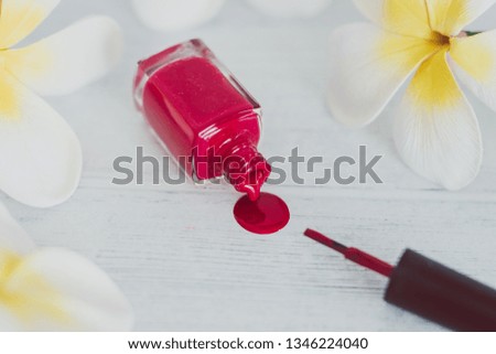 red nail polish bottle spilling color on wooden surface with flowers around it, concept of cosmetics industry and manicure 