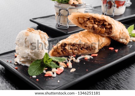 apple strudel served with ice cream on a flat black plate. Delicious dessert on a black background close-up
