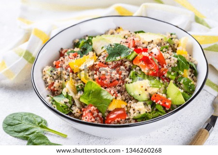 Quinoa salad with spinach, avocado, paprika and tomatoes on white stone table.