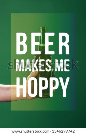 cropped view of man holding beer bottle near beer makes me hoppy lettering on green background