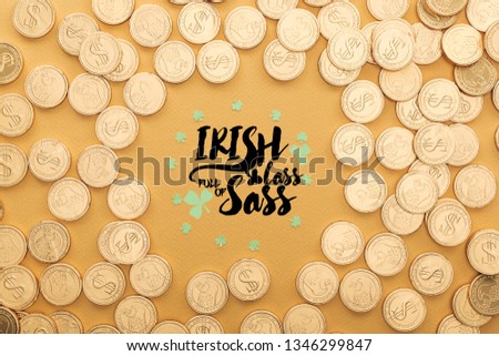 top view of golden coins with dollar signs and circle of shamrocks near lettering on orange background
