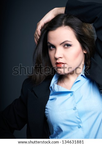 Attractive young woman in a blue shirt and black jacket. Hair in motion. On a gray background