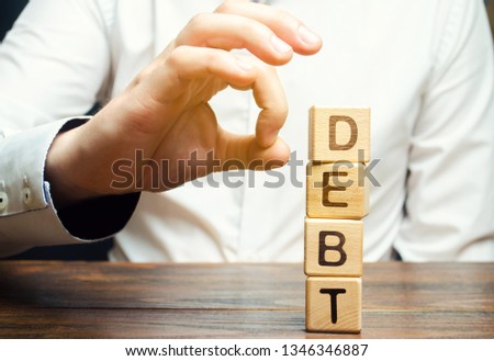 Businessman removes wooden blocks with the word Debt. Reduction or restructuring of debt. Bankruptcy announcement. Refusal to pay debts or loans and invalidate them. Debts service relief Royalty-Free Stock Photo #1346346887