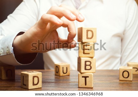 Businessman removes wooden blocks with the word Debt. Reduction or restructuring of debt. Bankruptcy announcement. Refusal to pay debts or loans and invalidate them. Debts service relief Royalty-Free Stock Photo #1346346968
