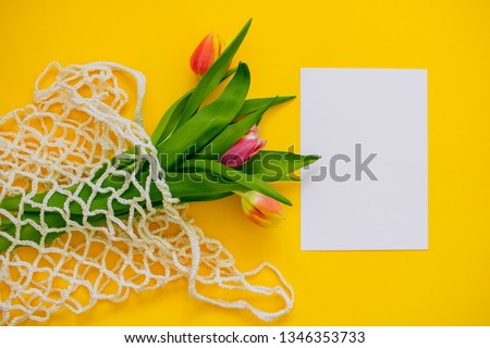 Spring bouquet of multicolored tulips in eco bag on a yellow background. Copy space, flat lay background.