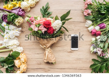 Fresh flowers and smartphone with blank screen on wooden surface
