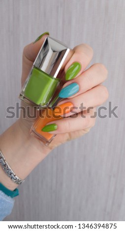 A female hand with long nails holds a bottle of green nail polish