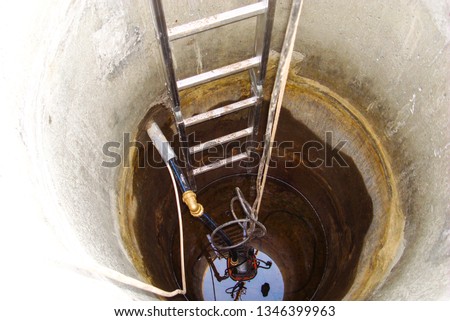 Concrete well for water. Extraction of groundwater. Submersible centrifugal pump pumps water. Concrete rings. Stairs. Tee pnd compression 32x32x32 mm brass. Water intake. Water supply in the house. Royalty-Free Stock Photo #1346399963