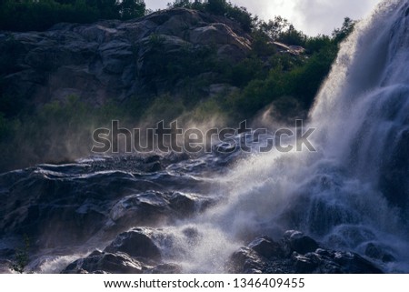 The rays of the sun through the clouds illuminate the spray from the waterfall.
