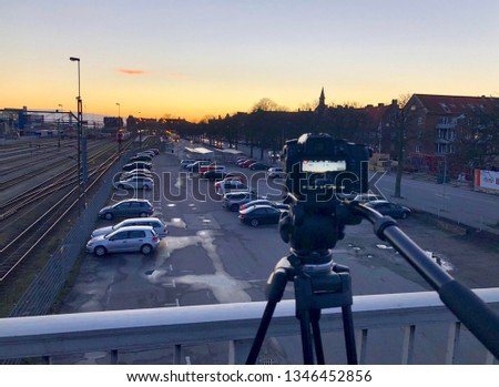 DSLR Camera On a Tripod on a Bridge Taking a Time Lapse of The Town Called Ystad in South Sweden Skane with Lots of Cars at a Parking Next To a Road and a Train Station Near The Harbour In The Evening