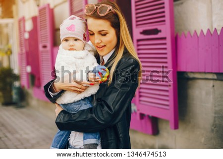 a young and stylish mother with light hair and a black leather jacket standing along with her little sweetheart in the spring city near building