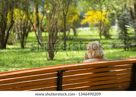 Mature woman with smartphone sitting on a bench in the spring park. Back view picture