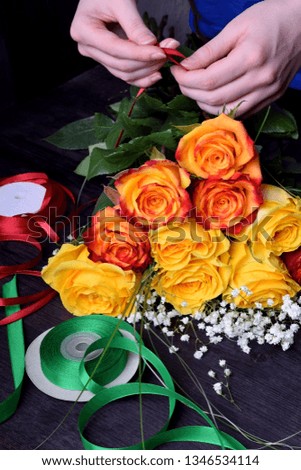 Florist is composing a bouquet of yellow and orange roses and gypsophila flowers. Satin ribbons next to it