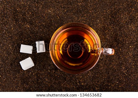 Cup of tea standing on dried leafs with lump sugar