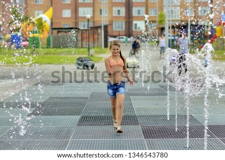Teenage girl fun running between the fountains in the Park in the summer.