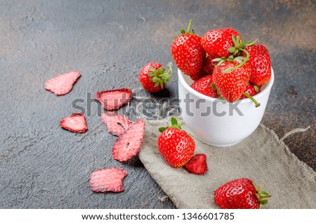 Ripe fresh strawberries in white mug and dry slised strawberry fruit chips on dark concrete background, copy space, healthy food concept