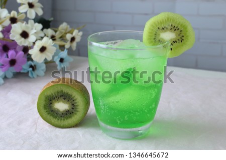 Green soda with ice and sliced kiwi in glass.