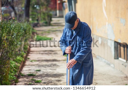 Man with a blue hat is cleaning pathway with a broomstick