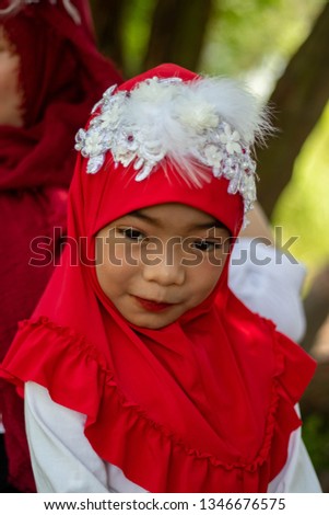 Muslim girls, islamic girls, wearing a red fabric head covering adorn with white fabric flowers red lip wear shirt white pants blue standing  photography on the chair prepare before to ramadan month.