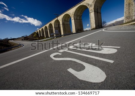 Stop Signal in a Crossroad . Foreground of a Stop Signal Painted on Ground at a Crossroad with a Bridge at Bottom