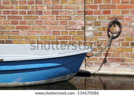 A blue rowing boat is docked at a brick wall