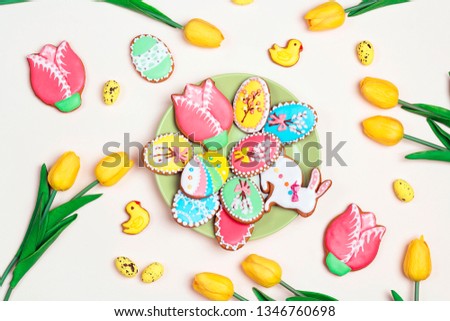 Easter homemade gingerbread cookies on the plate on a light background with tulips. Gingerbread in shape of easter bunny and easter eggs.
