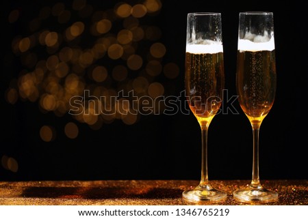 Glasses of champagne and golden glitter on table against blurred background. Space for text