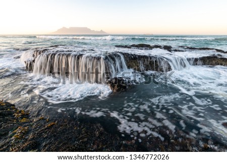 Beautiful view of streaming water over rocks in the ocean with table mountain in the background in early morning golden light