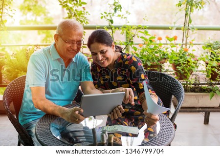 Senior Indian/asian couple accounting, doing home finance and checking bills with laptop, calculator and money while sitting on sofa/couch or dining table at home Royalty-Free Stock Photo #1346799704