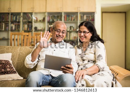 Indian/asian Senior couple video chatting on tablet/computer while sitting at couch or in garden at home, selective focus
 Royalty-Free Stock Photo #1346812613