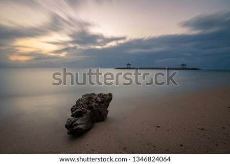 natural Long exposure on the beach, the sea is calm and a stone as a detail draws the picture, in the water you can see two small temples. Beautiful sunrise on the island of Bali
