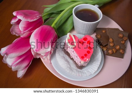 
On a wooden background, a tray with a cup of tea, chocolates, a heart-shaped cake and a beautiful bouquet of tulips.