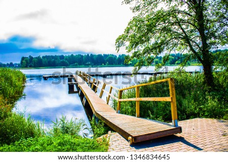 Beautiful lake park on a bright sunny summer day near Trakai Castle in Lithuania, Europe. Lake Galvė is a lake in Trakai Lithuania. Lake and Forest Panorama, blue sky, yellow boat dock.  Royalty-Free Stock Photo #1346834645