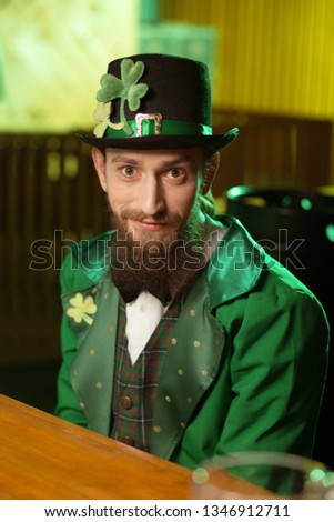 Before the party. Dark-haired bearded young man wearing a green costume sitting at the table in a cafe