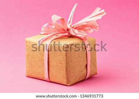 Gift box in craft paper with pink ribbon and bow