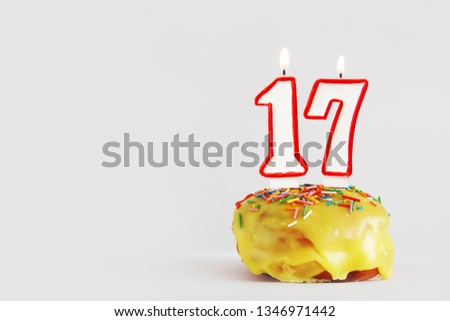 Seventeen  years anniversary. Birthday cupcake with white burning candles with red border in the form of number Seventeen. Light gray background with copy space