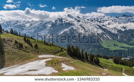 Switzerland, panoramic view on snow Alps with green hills and clouds