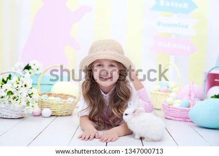 Easter! Little Girl is playing with Easter bunny. Easter colorful decor, basket of colorful eggs. Baby chasing Easter eggs. Agriculture. Child and garden. Little farmer. child plays with fluffy rabbit