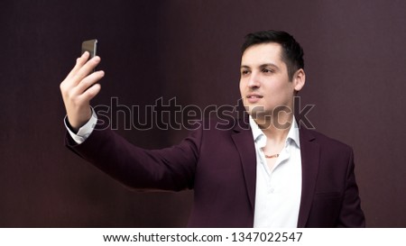 A man in a suit takes pictures of himself. Young man making selfie photo on smartphone.