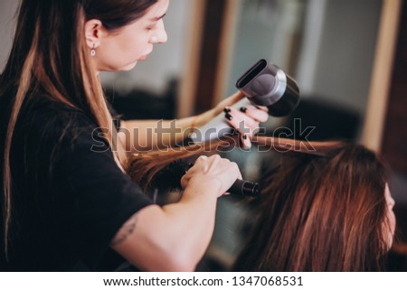Hairdresser drying hair to a girl and doing her hairdo in a beauty salon