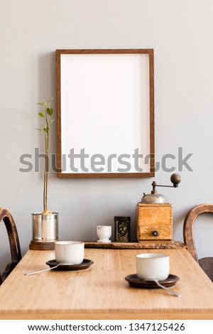 Stylish and modern interior design of kitchen space with small wooden table with mock up photo frame, avocado plant, accessories and cups of coffee. Scandinavian and cozy room decor.