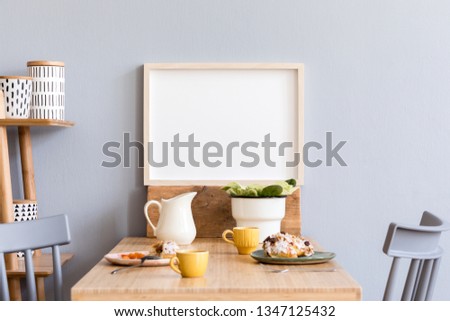 Stylish and modern interior of kitchen space with small wooden table with mock up photo frame, plants, design cups, furnitures and tasty dessert. Scandinavian room decor with kitchen accessories.