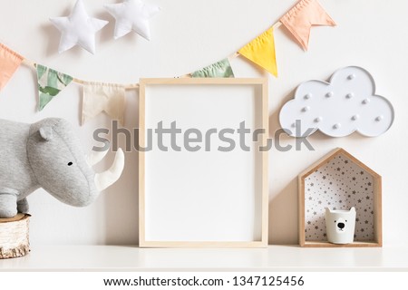 The modern scandinavian newborn baby room with mock up photo frame, wooden toy, plush rhino and clouds. Hanging cotton flags, white stars and cloud. Minimalistic and cozy decor of childroom.