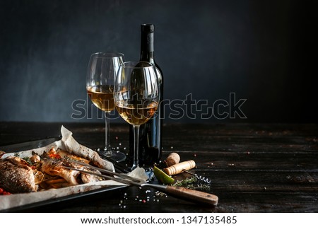 dinner concept for two. two glasses of white wine, baked fish.