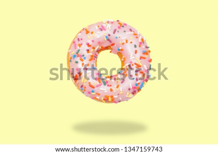 Pink donut with icing on pastel yellow background.