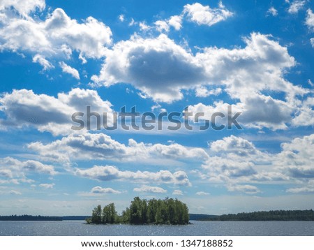 Small island  ]covered by green spruce forest under bright blue sky with clouds on Ladoga lake. View from water on shore at sunny summer day. Karelia region, Russia.