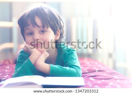 Pensive boy looks into the book. The child is reading. Portrait of a cute kid. The boy lies on the couch and looks at the picture in the book.