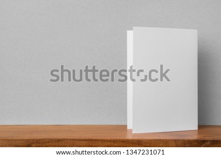 Design concept - front view of greeting card on bookshelf and grey wall for mockup, not 3D render
