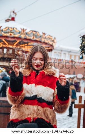 Stylish girl having fun on Red Square through winter Holiday festival with sparkles in her arms