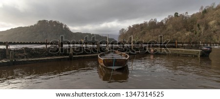 Boat in Loch Lomond tied up to dock with view of Balmaha in the background Royalty-Free Stock Photo #1347314525
